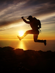 Silhouette of person jumping over mountain at sunset, symbolizing the triumph of overcoming challenges.